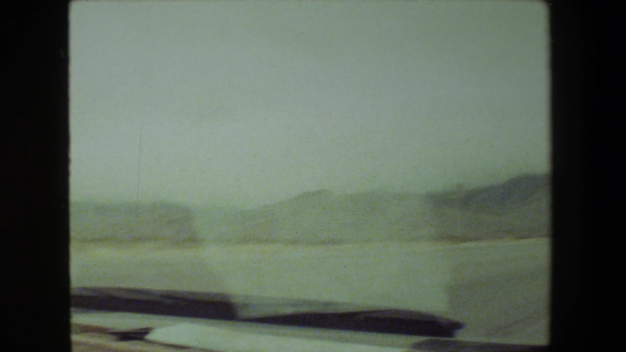 A 1981 Malibu-area 8mm road-trip frame appears to show hazy rolling hills and roadside terrain viewed from inside a moving vehicle.