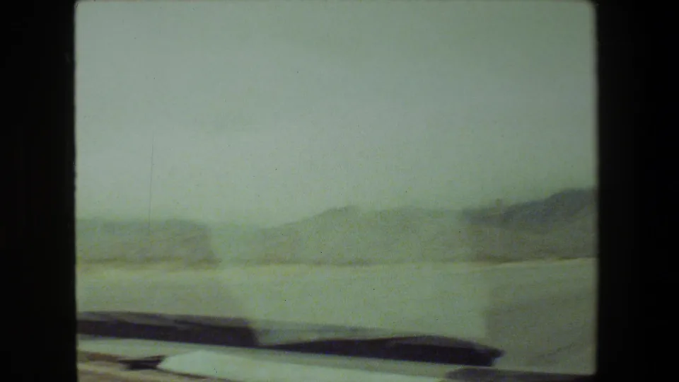 A 1981 Malibu-area 8mm road-trip frame appears to show hazy rolling hills and roadside terrain viewed from inside a moving vehicle.