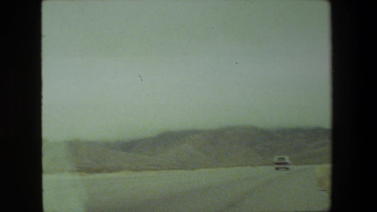Distant white car on a roadway with hazy hills beyond.