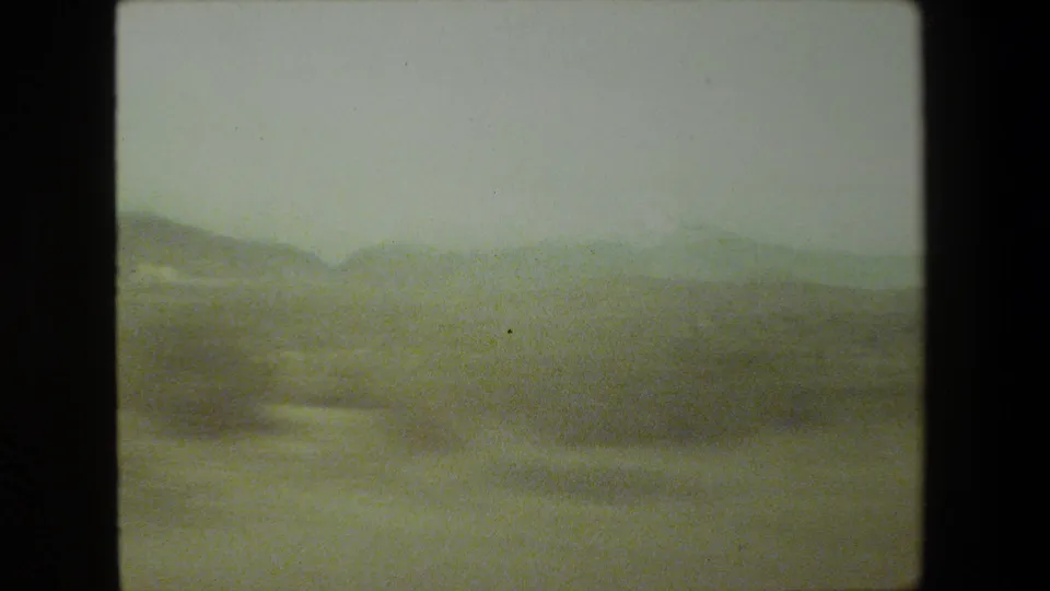 A faded 8mm frame from the Malibu-area road trip shows hazy scrubland and low hills through vehicle-motion blur.