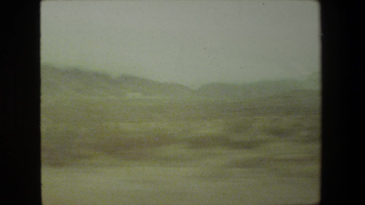 1981 Malibu-area home-movie frame showing a soft, hazy mountain landscape through a moving vehicle viewpoint, with heavy grain and dark 8mm frame edges.