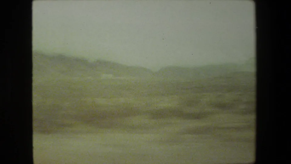 1981 Malibu-area home-movie frame showing a soft, hazy mountain landscape through a moving vehicle viewpoint, with heavy grain and dark 8mm frame edges.