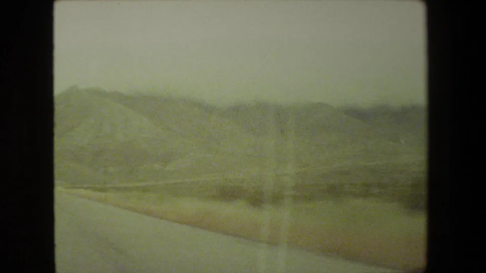Soft 8mm frame showing a mountain slope and roadside edge from inside a moving car in the 1981 Malibu travel footage.
