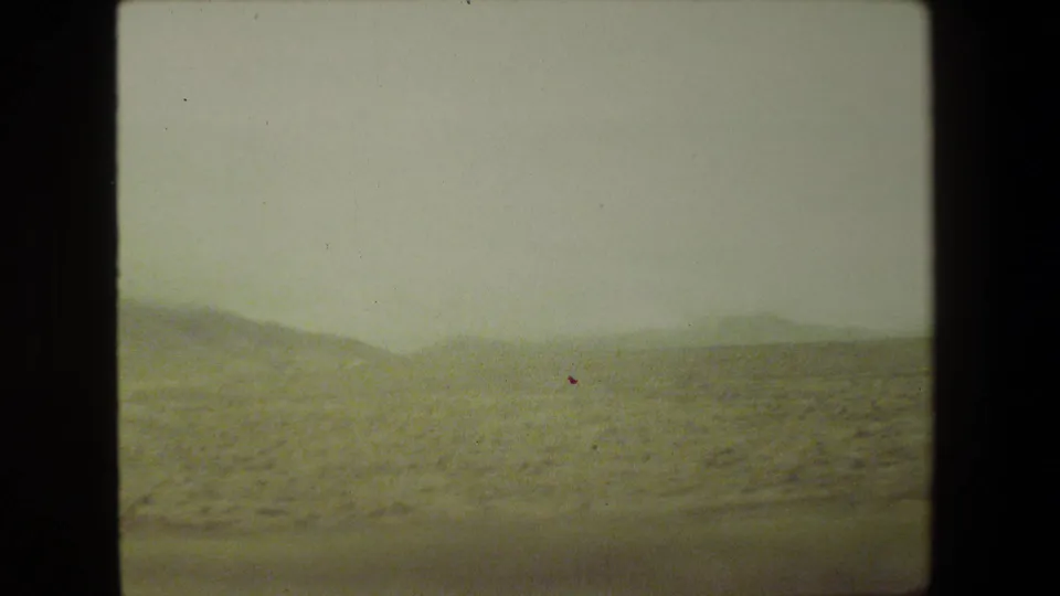 1981 Malibu 8mm frame with pale sky, dry hills, and scrub vegetation viewed from a moving road trip perspective.