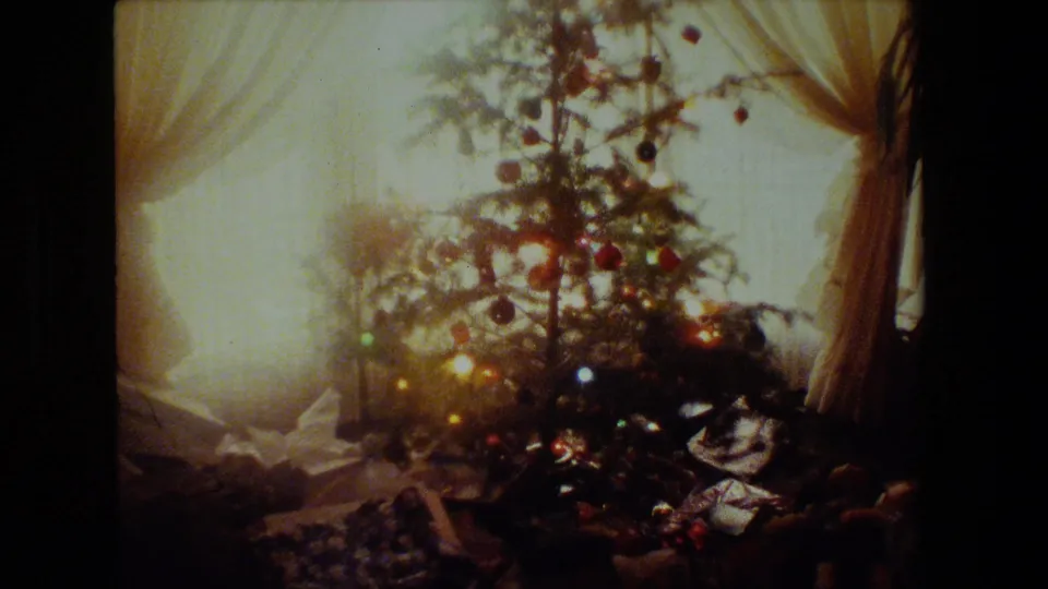 A 1981 Malibu holiday interior frame shows a lit Christmas tree against bright curtained windows, with ornaments and wrapped presents visible near the base.