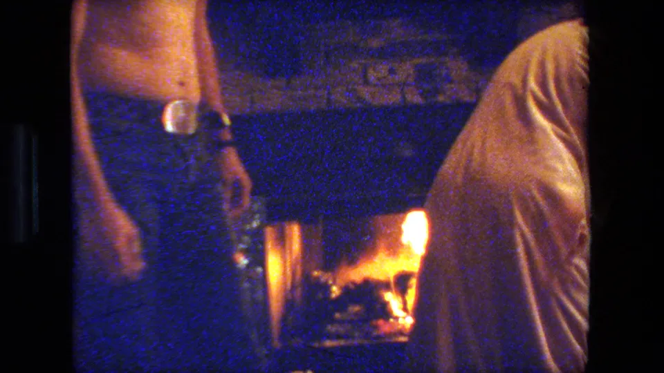 In the same 1981 Malibu Christmas interior, an adult man stands close to a glowing fireplace while a covered seated figure occupies the foreground.