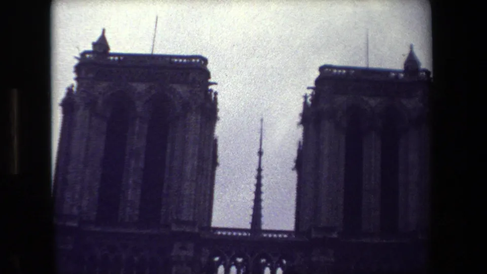1981 Paris 8mm frame showing Notre-Dame Cathedral's twin towers and central spire in dark silhouette beneath an overcast sky.