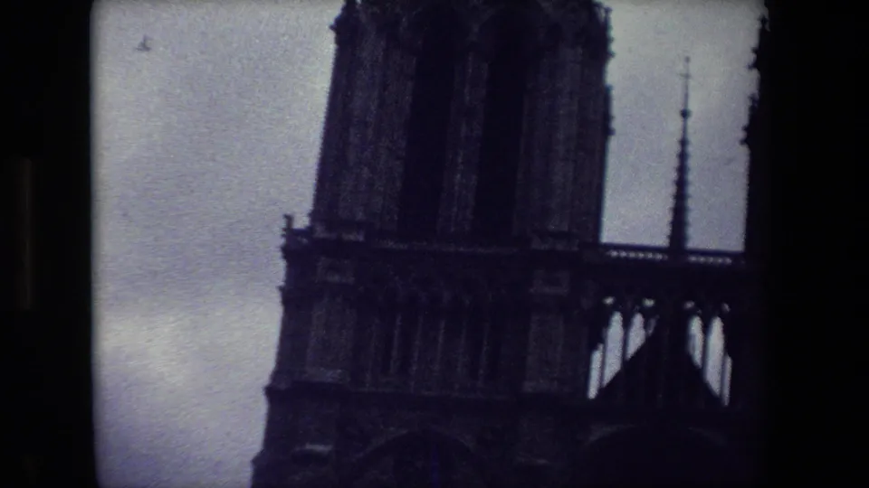 1981 Paris 8mm frame showing Notre-Dame's tower, central spire, upper facade, and lower Gothic arches in a dark blue-toned exposure.