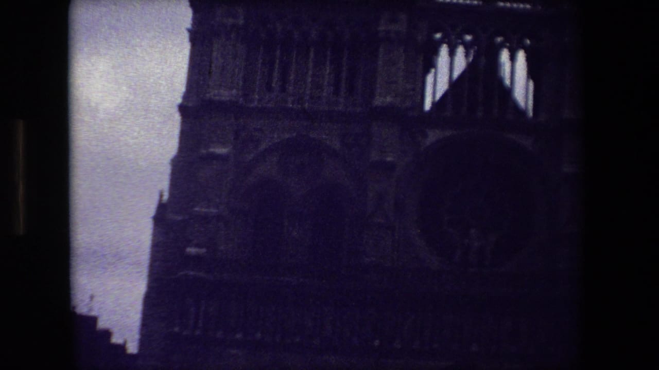 Dark 1981 Paris 8mm frame showing the upper portion of a Gothic cathedral facade, with arched stonework and a pale dim sky along the left edge.