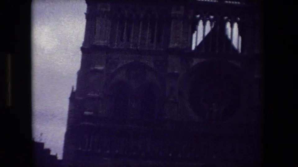 Dark 1981 Paris 8mm frame showing the upper portion of a Gothic cathedral facade, with arched stonework and a pale dim sky along the left edge.