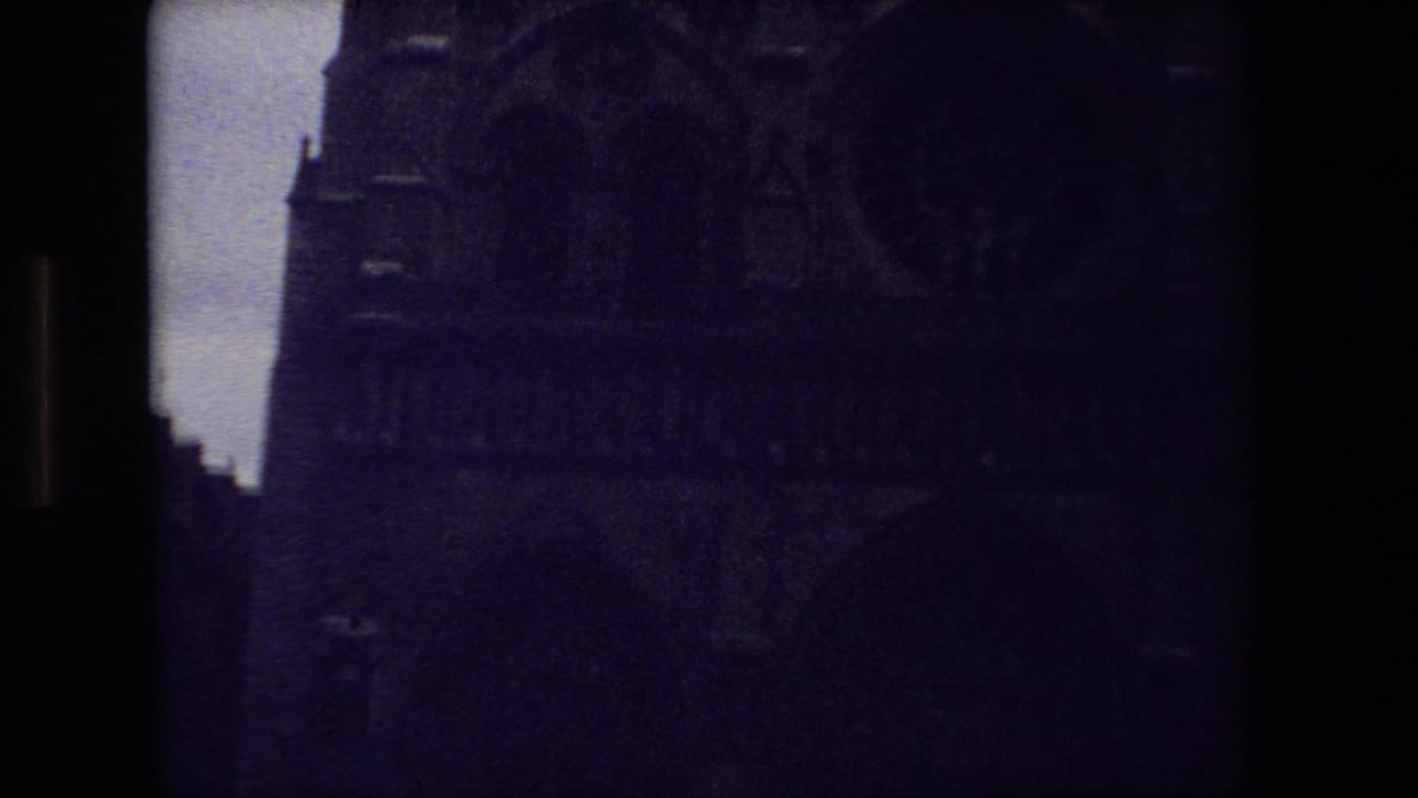 Very dark 1981 Paris 8mm frame with the upper facade of a Gothic cathedral, where stone arches and vertical window shapes are faintly visible.