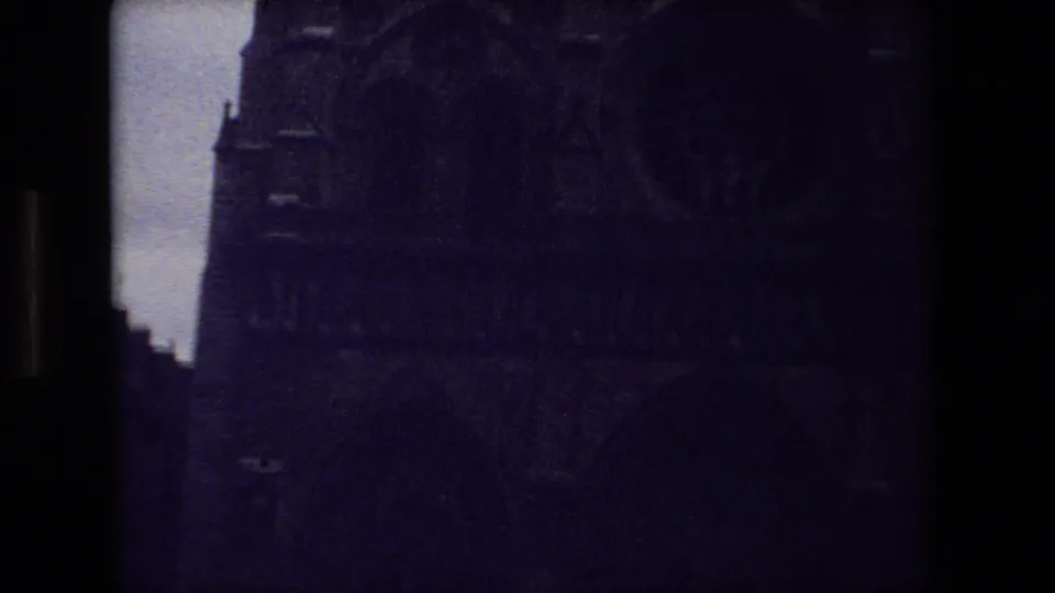 Very dark 1981 Paris 8mm frame with the upper facade of a Gothic cathedral, where stone arches and vertical window shapes are faintly visible.