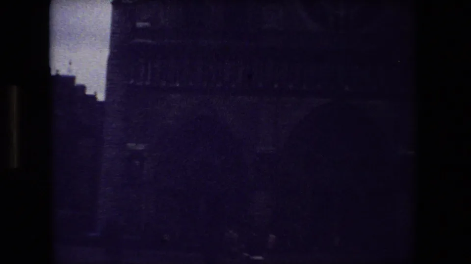 Underexposed 1981 Paris 8mm frame showing a lower portion of the Gothic cathedral facade, with a stepped silhouette and pale sky visible along the left side.