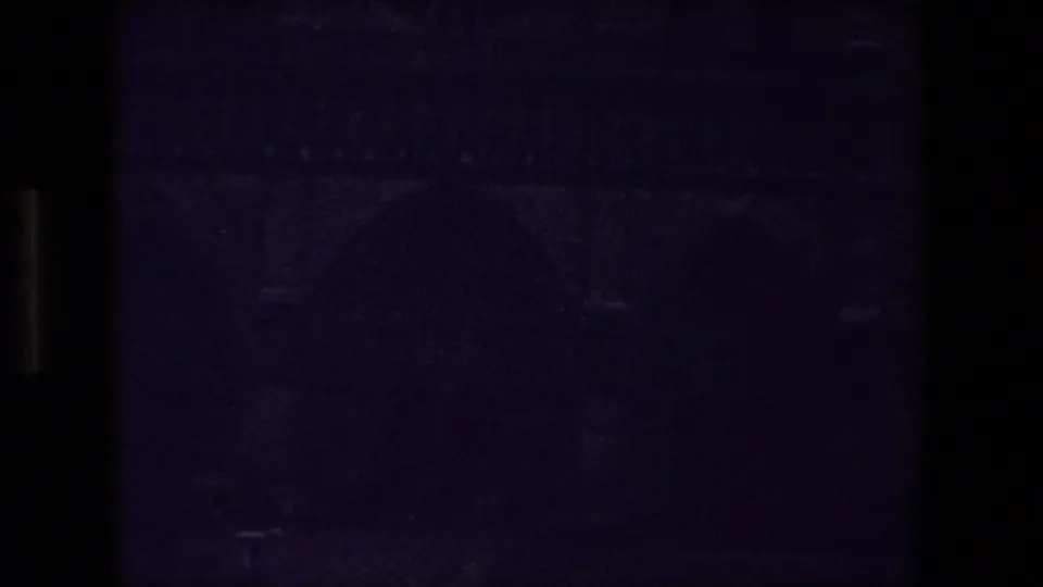 Dark final 1981 Paris 8mm frame of a Gothic cathedral exterior, with faint arch forms and stone facade details softened by grain and low light.