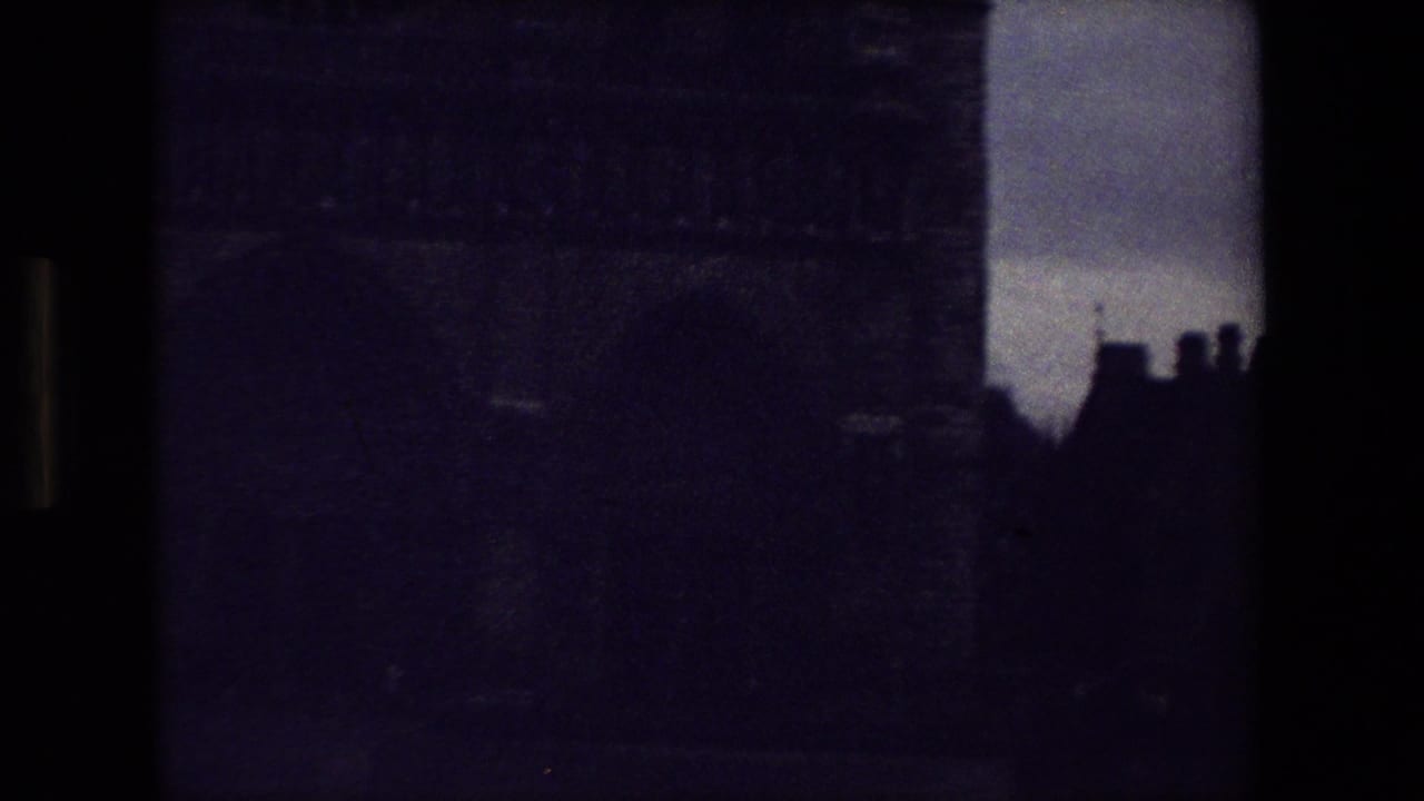 Soft-focus 1981 Paris 8mm frame showing dark masonry, silhouetted rooflines, and cloudy sky near a cemetery or churchyard setting.