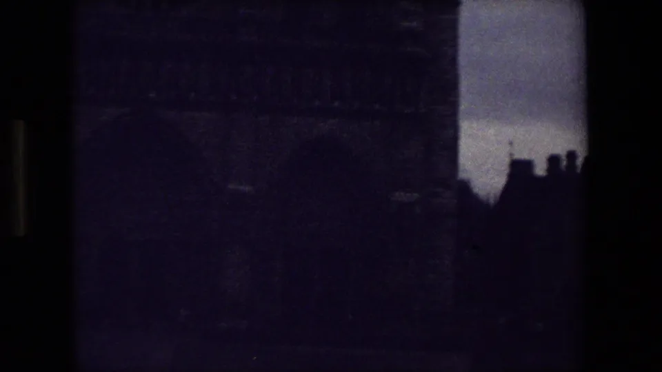 Soft-focus 1981 Paris 8mm frame showing dark masonry, silhouetted rooflines, and cloudy sky near a cemetery or churchyard setting.