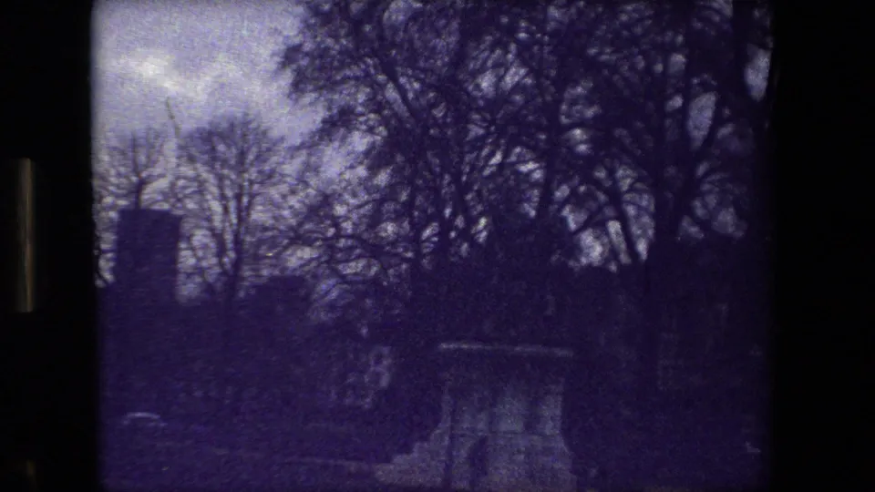 Soft, purple-tinted 1981 Paris 8mm frame showing a stone cemetery monument surrounded by bare trees and shadowed graveyard grounds.