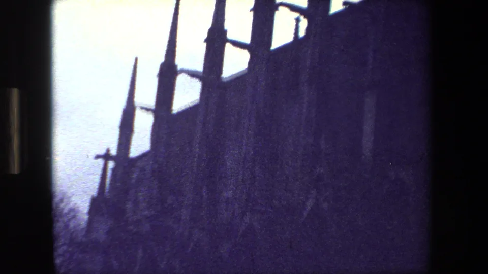 In supplied 1981 Paris 8mm footage, tall Gothic-style spires and a dark roofline appear in silhouette against a pale sky with purple film tint.