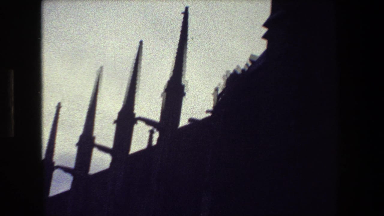 A low-angle 8mm frame from the supplied Paris clip shows several pointed spires rising above a dark Gothic-style roofline against a bright sky.