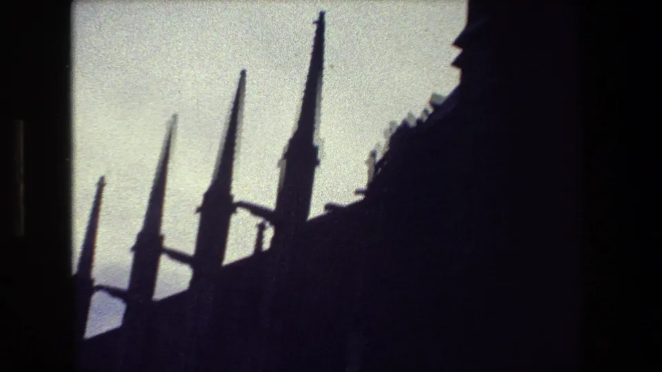 A low-angle 8mm frame from the supplied Paris clip shows several pointed spires rising above a dark Gothic-style roofline against a bright sky.