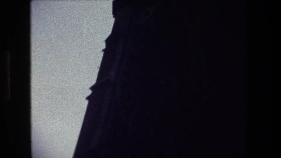A very dark, close 8mm frame shows the side of a Gothic-style structure with pointed roof details silhouetted against the sky in the supplied Paris clip.