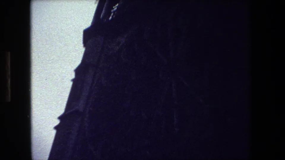 Low-angle 1981 Paris 8mm frame showing a shadowed Gothic church wall or tower edge silhouetted against a bright pale sky.