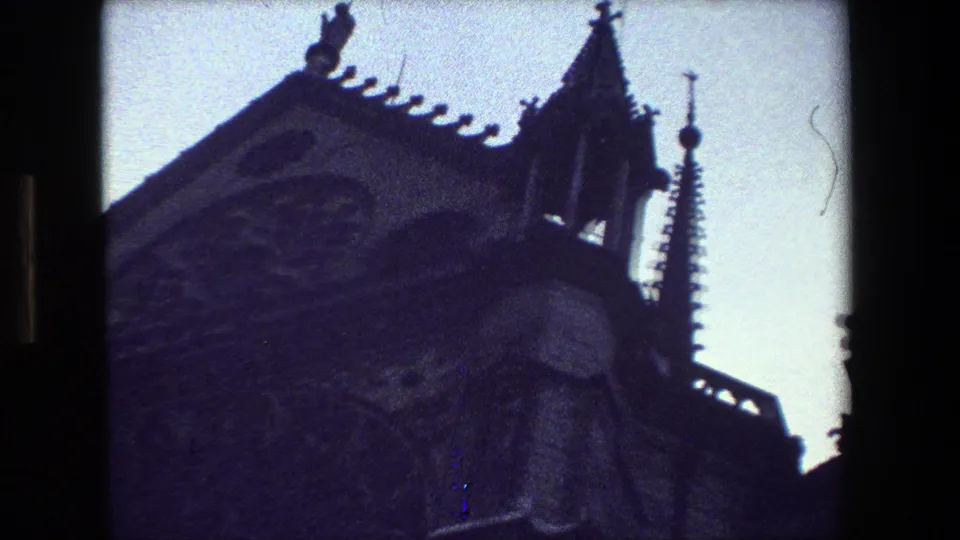 1981 Paris 8mm frame of a Gothic church corner with pointed spire, carved roof edge, and dark stonework viewed from below.
