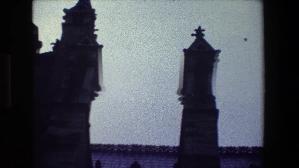 Low-angle 1981 Paris 8mm frame showing two narrow Gothic tower or spire elements rising above a roofline against a pale sky.