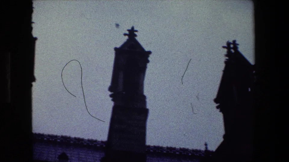 1981 Paris 8mm frame showing dark ornate spires and a roofline silhouetted against a pale sky, with visible film grain and edge shadowing.