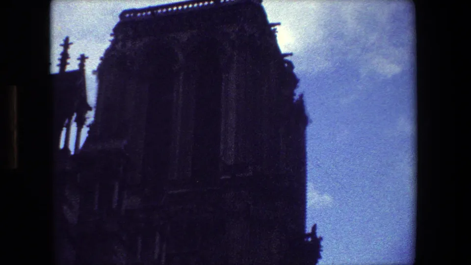 1981 Paris 8mm frame showing a low-angle view of a shadowed Gothic cathedral facade with vertical stone details silhouetted against blue sky.