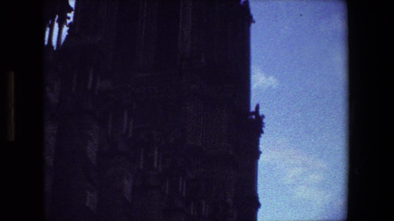 1981 Paris 8mm frame with the cathedral facade filling most of the view, its stonework mostly in shadow beside pale blue sky and cloud.