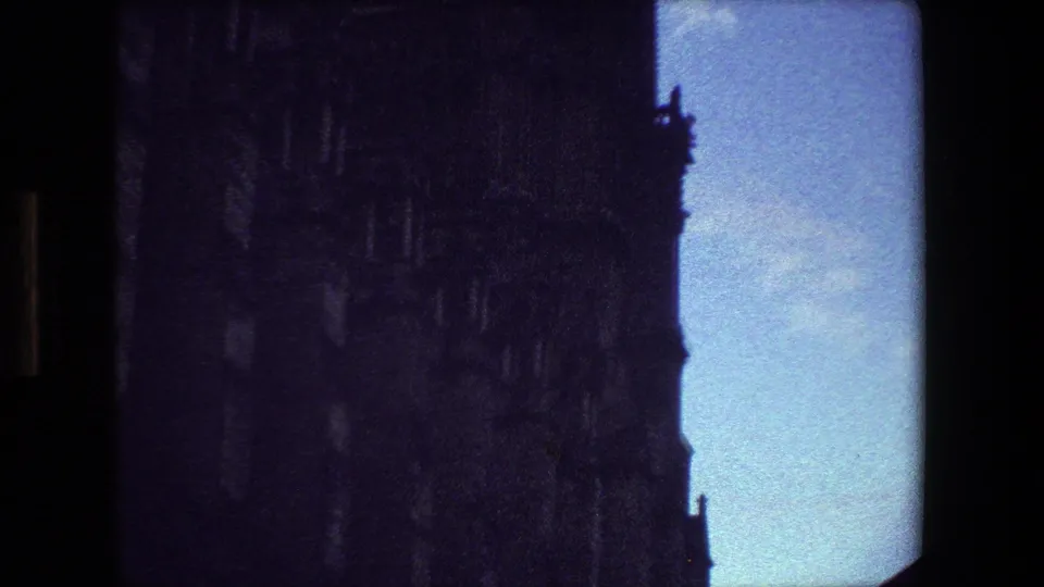 1981 Paris 8mm frame showing a tightly cropped, low-angle section of a Gothic cathedral facade with shadowed ornament and blue sky at the side.