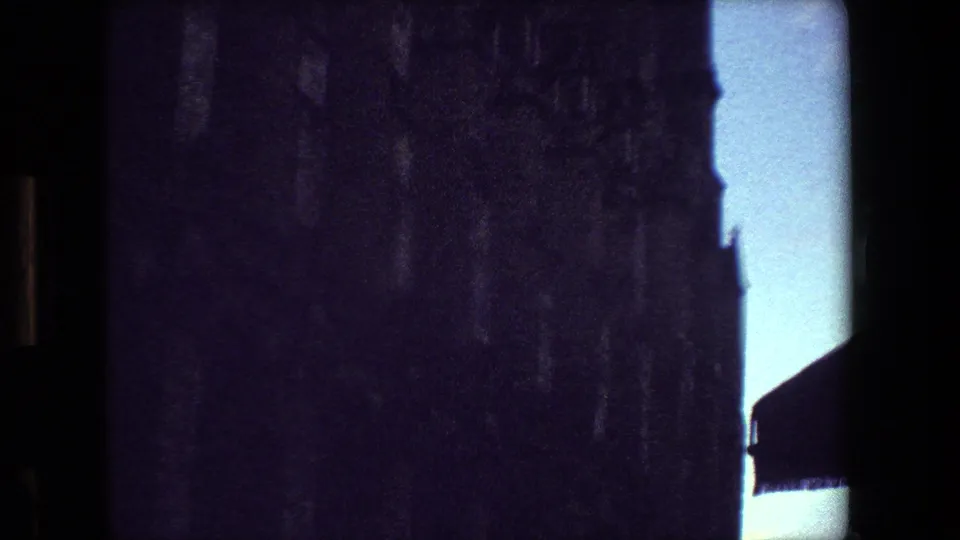 1981 Paris 8mm frame showing the cathedral facade in deep shadow against bright blue sky, with a small roof or awning edge visible at the lower right.