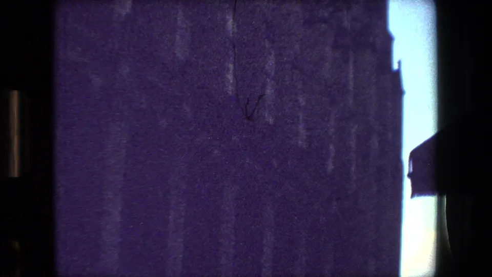 Purple-tinted 8mm frame from the supplied 1981 Paris clip, looking from a dark interior toward bright window gaps and faint exterior shapes.
