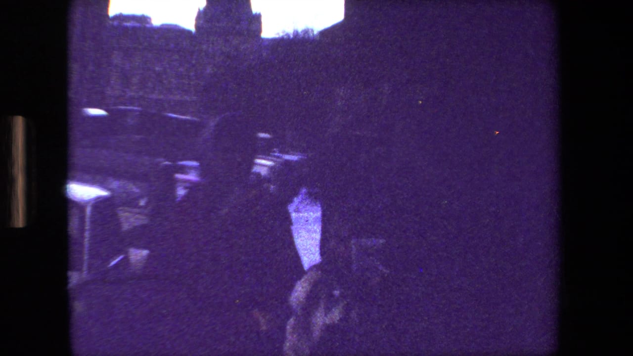 A silhouetted figure stands near the center of a dim, purple-tinted 1981 Paris 8mm frame, with parked cars and dark building edges in the background.