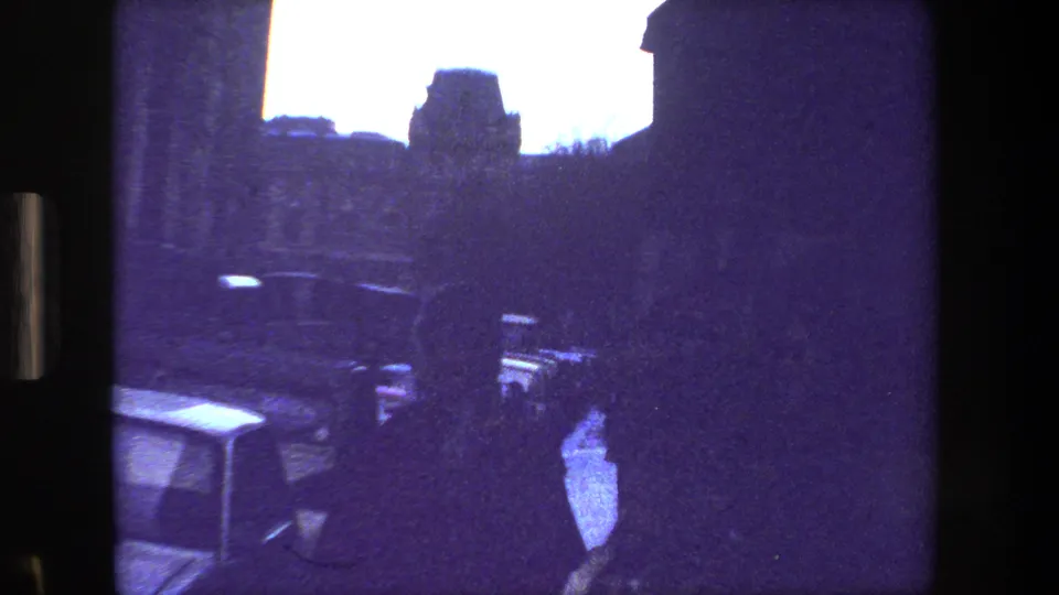 The final frame shows a silhouetted person centered in a dim Paris street or courtyard view, framed by dark architecture and nearby parked cars on aged 8mm film.
