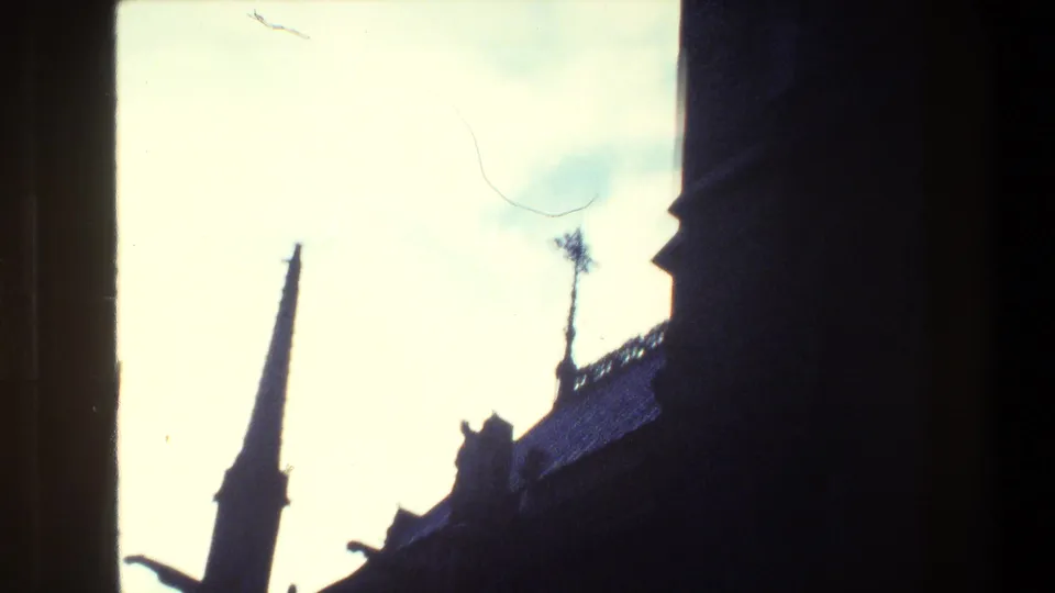 Paris 1981 8mm frame showing a narrow Gothic-style spire and dark roofline silhouetted against a bright pale sky.