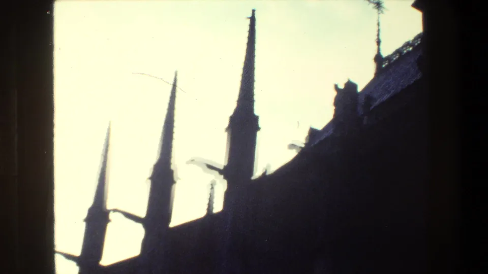 Paris 1981 8mm frame with several Gothic-style spires, projecting roof details, and a dark architectural silhouette beneath a washed-out sky.