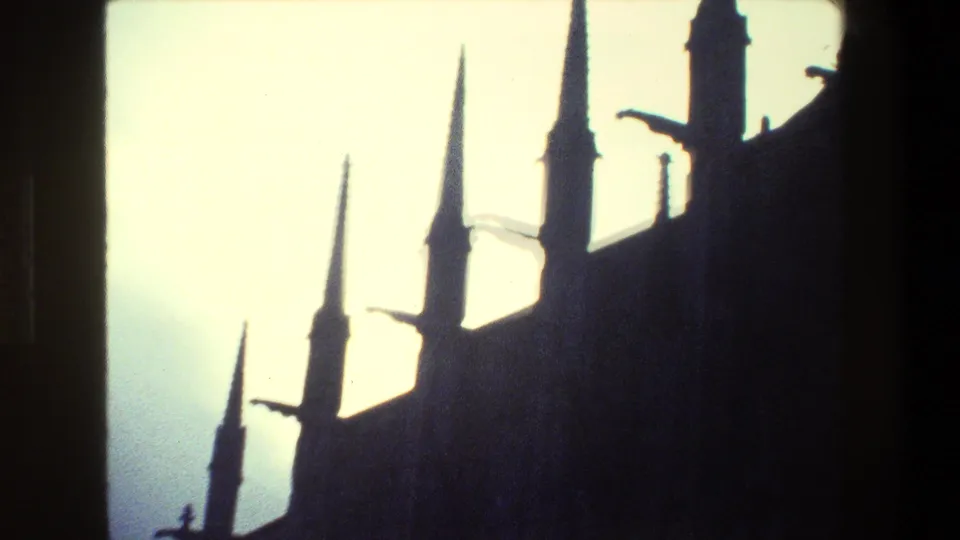 Paris 1981 8mm frame showing a cathedral-like Gothic roofline with several pointed spires and small projecting details in deep silhouette.