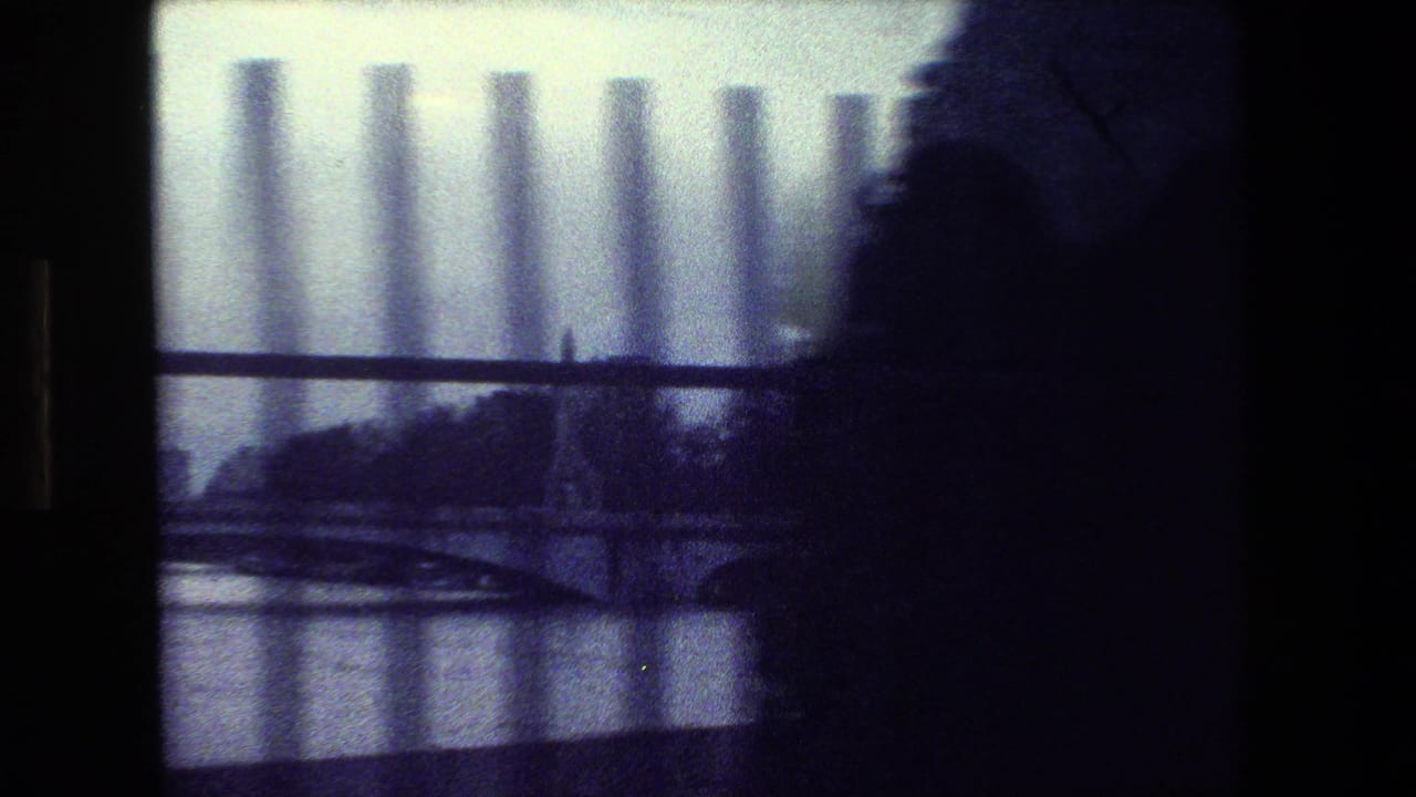 Blurred riverside bridge and fence bars with a dark foreground silhouette at right.