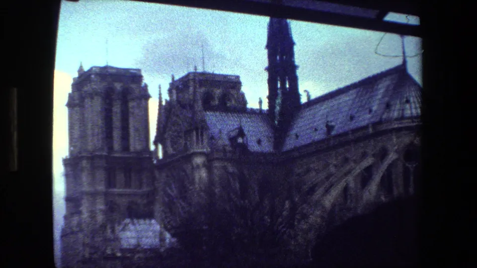 1981 Paris frame showing Notre-Dame Cathedral's towers, spire, roof, and upper Gothic structure from a close visitor viewpoint.