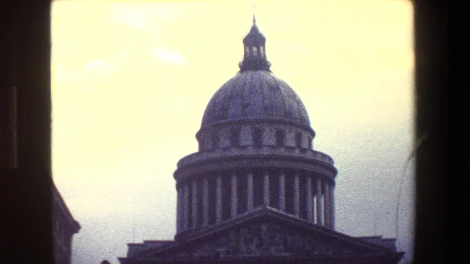 Vintage 8mm frame from Paris showing a domed classical building with a columned facade, triangular pediment, and pale overcast sky.