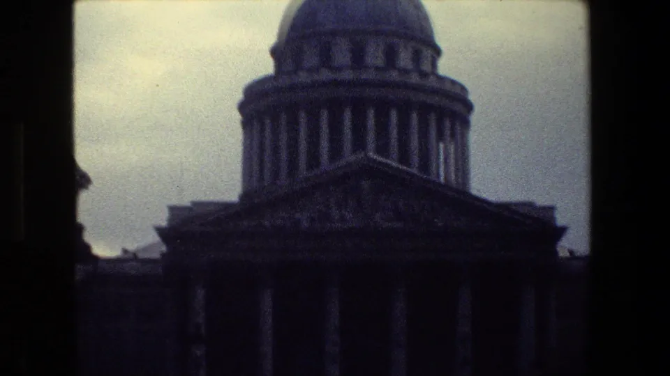 Soft, grainy 8mm view of a Paris domed classical building with a ring of columns, a shadowed pediment, and cloudy sky above.