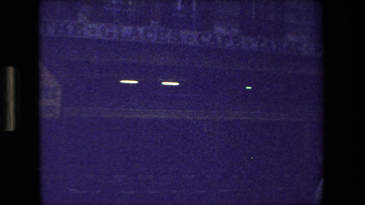 Dark street scene with several small distant lights against a blue-purple frame.