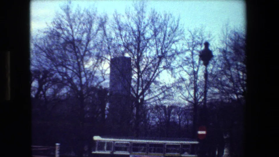 1981 Paris 8mm frame with bare trees, street barriers, a no-entry sign, and silhouetted street furniture against a pale blue sky.