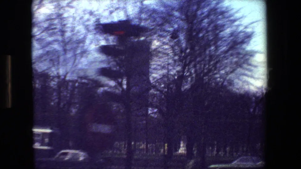 Paris street scene from a moving 8mm camera, showing a red traffic light, winter trees, cars, and a tall building partly obscured by blur.