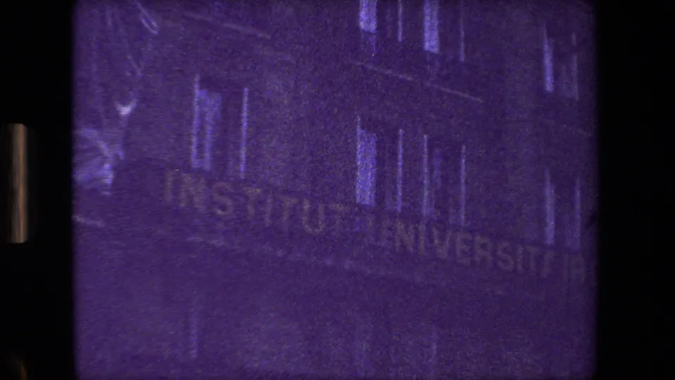 Paris building exterior with the sign "INSTITUT UNIVERSITAIRE" partly visible, filmed in soft, grainy 8mm with a strong purple cast.