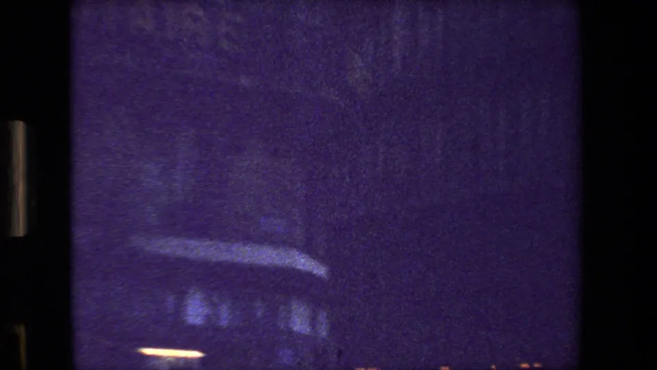 Low, passing 8mm view of a dark Paris street surface and blurred vehicle or curb detail, with heavy grain and purple-blue color distortion.