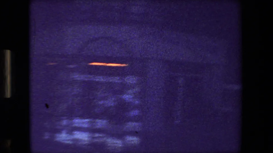 Grainy final Paris drive-by frame with a blurred vehicle, small orange light streak, dark building facade, and faint institutional sign detail.