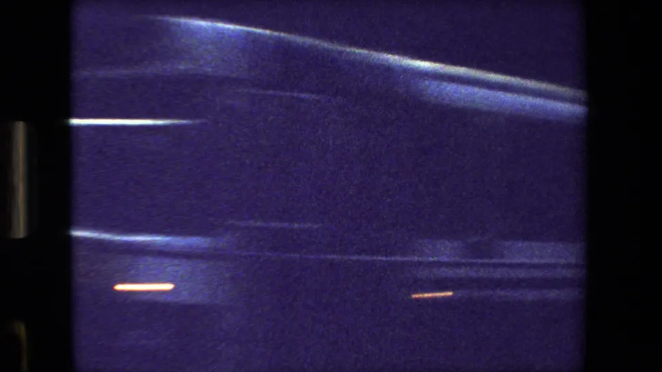 Purple-blue 8mm frame from Paris, France in 1981 showing a close, blurred view of a passing bus or large vehicle seen through glass.